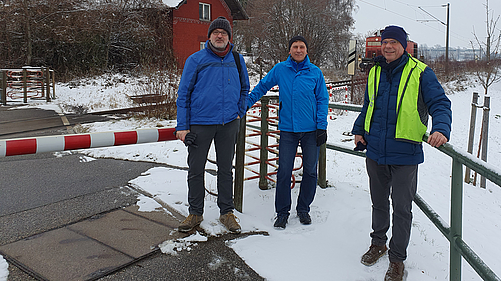 Drei ÖDP-Aktive aus Landshut Stadt stehen vor dem alten Ergoldinger Bahnhaltepunkt, als gerade eine kleine Lok einfährt